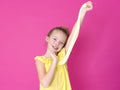 Beautiful 10 year old girl is playing with yellow slime in front of pink background and is happy