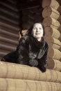 A beautiful 45-year-old woman with red hair poses on the veranda of a log house.