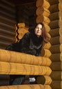 A beautiful 45-year-old woman with red hair poses on the veranda of a log house.