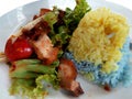 Beautiful yellow and blue rice, crispy pork, stir-fried chilies and fresh salad on a white plate