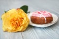 a beautiful yellow rose with an opened bud and a donut with pink icing on a white ceramic plate on a gray wooden background. Royalty Free Stock Photo