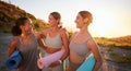 Beautiful yoga women bonding and holding yoga mats in outdoor practice in remote nature. Diverse group of young smiling