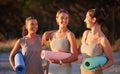 Beautiful yoga women bonding and holding yoga mats in outdoor practice in remote nature. Diverse group of young smiling
