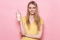 Beautiful young adult happy woman holding plastic bottle with clear water in hand standing near pink wall and smiling Royalty Free Stock Photo