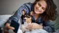 Beautiful young adult woman in pajamas doing selfie on smartphone with her dog bassengi in the morning in bed Royalty Free Stock Photo