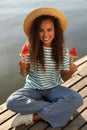 Beautiful young African American woman with pieces of watermelon on wooden pier near river Royalty Free Stock Photo