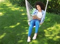 Beautiful young African-American woman reading book in hammock outdoors Royalty Free Stock Photo