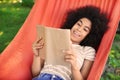 Beautiful young African-American woman reading book in hammock outdoors Royalty Free Stock Photo