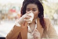 Beautiful young african american woman sitting in outdoor cafe and drinking coffee Royalty Free Stock Photo