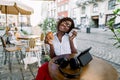 Beautiful young African American woman, sitting in outdoor city cafe, holding paper coffee cup and fresh tasty croissant Royalty Free Stock Photo