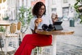 Beautiful young african american woman wearing striped shirt and red pants, drinking takeaway coffee and eating Royalty Free Stock Photo