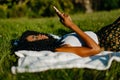 The beautiful young african girl with green eye shadows is laying on the grass and chatting, texting and browsing via