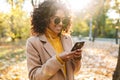 Beautiful young african happy woman walking outdoors in a spring park using mobile phone listening music with earphones Royalty Free Stock Photo