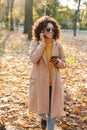 Beautiful young african happy woman walking outdoors in a spring park using mobile phone listening music with earphones Royalty Free Stock Photo