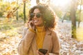 Beautiful young african happy woman walking outdoors in a spring park using mobile phone listening music with earphones Royalty Free Stock Photo