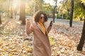 Beautiful young african happy woman walking outdoors in a spring park using mobile phone listening music with earphones Royalty Free Stock Photo