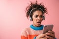 Beautiful young african woman posing isolated over pink wall background listening music with headphones using mobile phone Royalty Free Stock Photo