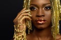 Beautiful young african woman posing at studio in golden jewellery, face with hand portrait over dark background Royalty Free Stock Photo