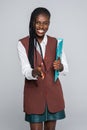 Beautiful young Afro American business woman in formal wear is holding a folder, looking at camera and smiling on gray background Royalty Free Stock Photo