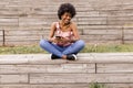 Beautiful young afro american woman using mobile phone, Sitting on wood stairs and smiling. wood background. Lifestyle outdoors Royalty Free Stock Photo