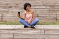 Beautiful young afro american woman using mobile phone, Sitting on wood stairs and smiling. wood background. Lifestyle outdoors Royalty Free Stock Photo