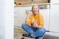 Beautiful young albino girl in casual clothes tasting delicious chocolate spread while sitting on the wooden floor in the domestic Royalty Free Stock Photo