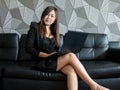 Beautiful young asia business woman sitting on sofa, working with laptop computer and wear black suit watching to camera and smile