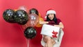 Beautiful young asia woman with santa hat and big giftbox sitting comfort with balloons happy new year. over red background. Royalty Free Stock Photo