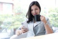 Beautiful young Asian businesswoman smiling holding a coffee mug and smartphone working at the office. Royalty Free Stock Photo