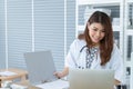 Beautiful young Asian female doctor feels happy, and smiling while working intently with laptop, computer on the desk in hospital Royalty Free Stock Photo