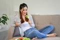 Beautiful Asian female having brunch in her living room, eating healthy green salad on couch Royalty Free Stock Photo