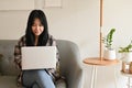 Beautiful young Asian female working from home, using laptop computer while sitting on sofa Royalty Free Stock Photo