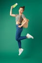 Beautiful young Asian girl traveler jumping in air while wearing bags and holding flight ticket, passport over green background Royalty Free Stock Photo