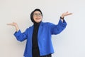 Beautiful young Asian Muslim woman in glasses, hijab and wearing blue blazer smiling confident and happy with both hands pointing Royalty Free Stock Photo