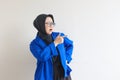 Beautiful young Asian Muslim woman in glasses, hijab and wearing blue blazer smiling confident and happy with both hands pointing Royalty Free Stock Photo