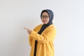 Beautiful young Asian Muslim woman in glasses, hijab and wearing yellow blazer with both hands pointing sideways and confused Royalty Free Stock Photo