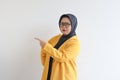 Beautiful young Asian Muslim woman in glasses, hijab and wearing yellow blazer with both hands pointing sideways and confused Royalty Free Stock Photo