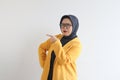 Beautiful young Asian Muslim woman in glasses, hijab and wearing yellow blazer with both hands pointing sideways and confused Royalty Free Stock Photo