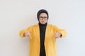 Beautiful young Asian Muslim woman in glasses, hijab and wearing yellow blazer sad expression with both hands pointing down Royalty Free Stock Photo