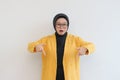 Beautiful young Asian Muslim woman in glasses, hijab and wearing yellow blazer shocked expression with both hands pointing down Royalty Free Stock Photo