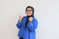 beautiful young Asian Muslim woman, wearing glasses and blue blazer with fists clenched in spirit gesture Royalty Free Stock Photo