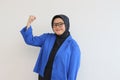 beautiful young Asian Muslim woman, wearing glasses and blue blazer with fists clenched in spirit gesture Royalty Free Stock Photo