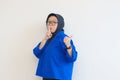 Beautiful young Asian Muslim woman, wearing glasses and blue blazer is pointing to the side with a do not make noise gesture Royalty Free Stock Photo