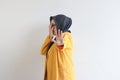 Beautiful young Asian Muslim woman, wearing glasses and yellow blazer covering 1 side of face with hand Royalty Free Stock Photo