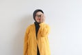 Beautiful young Asian Muslim woman, wearing glasses and yellow blazer covering 1 side of face with hand while smiling Royalty Free Stock Photo