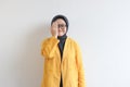 Beautiful young Asian Muslim woman, wearing glasses and yellow blazer covering 1 side of face with hand while smiling Royalty Free Stock Photo