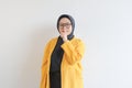 Beautiful young Asian Muslim woman, wearing glasses and yellow blazer with a do not make noise gesture Royalty Free Stock Photo