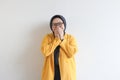 beautiful young Asian Muslim woman, wearing glasses and yellow blazer with happy face expression while covering mouth Royalty Free Stock Photo
