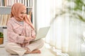 Beautiful young Asian Muslim woman wearing hijab using her laptop in her living room Royalty Free Stock Photo