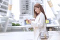 Beautiful young Asian professional working woman in a cream suit is using mobile phone smartphone to contact with partners while Royalty Free Stock Photo